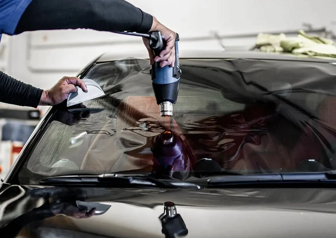 Person uses a power drill on a car windshield during auto body repair