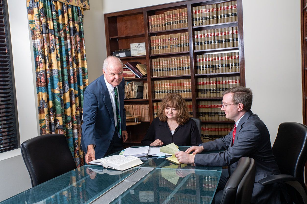 Three lawyers in a wood-paneled office reviewing documents at a table.