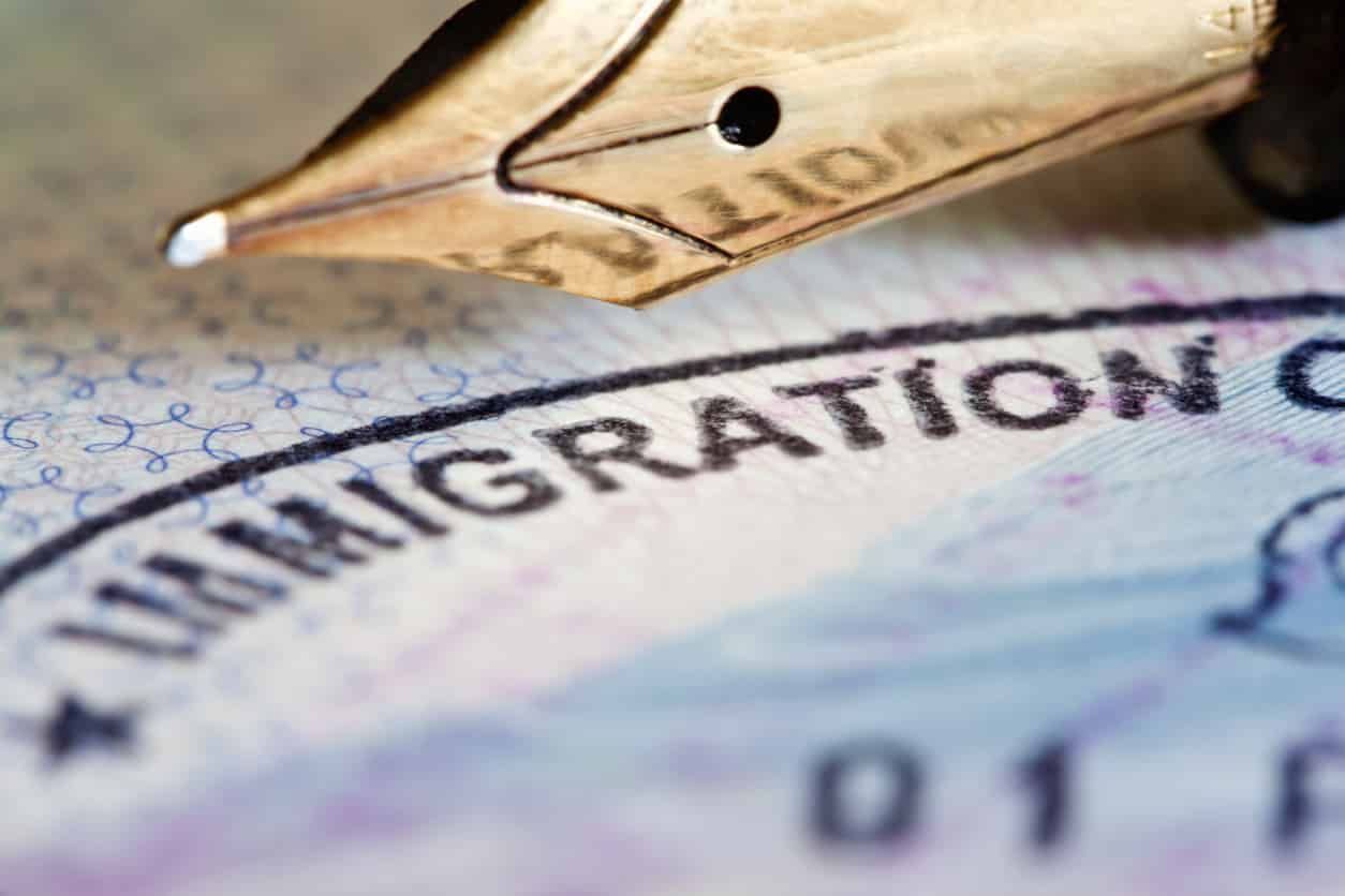Fountain pen tip over a blurry immigration stamp.