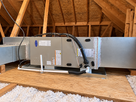 Attic HVAC unit with ductwork and insulation along wooden rafters