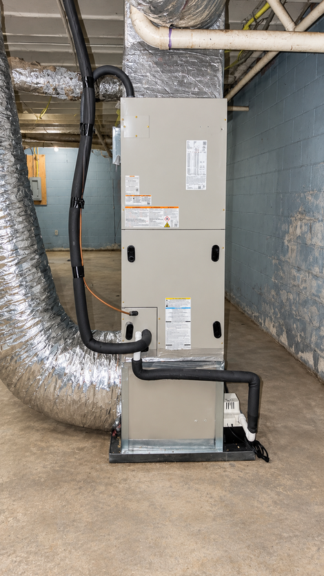 Gray HVAC furnace with silver ductwork in a basement utility room.