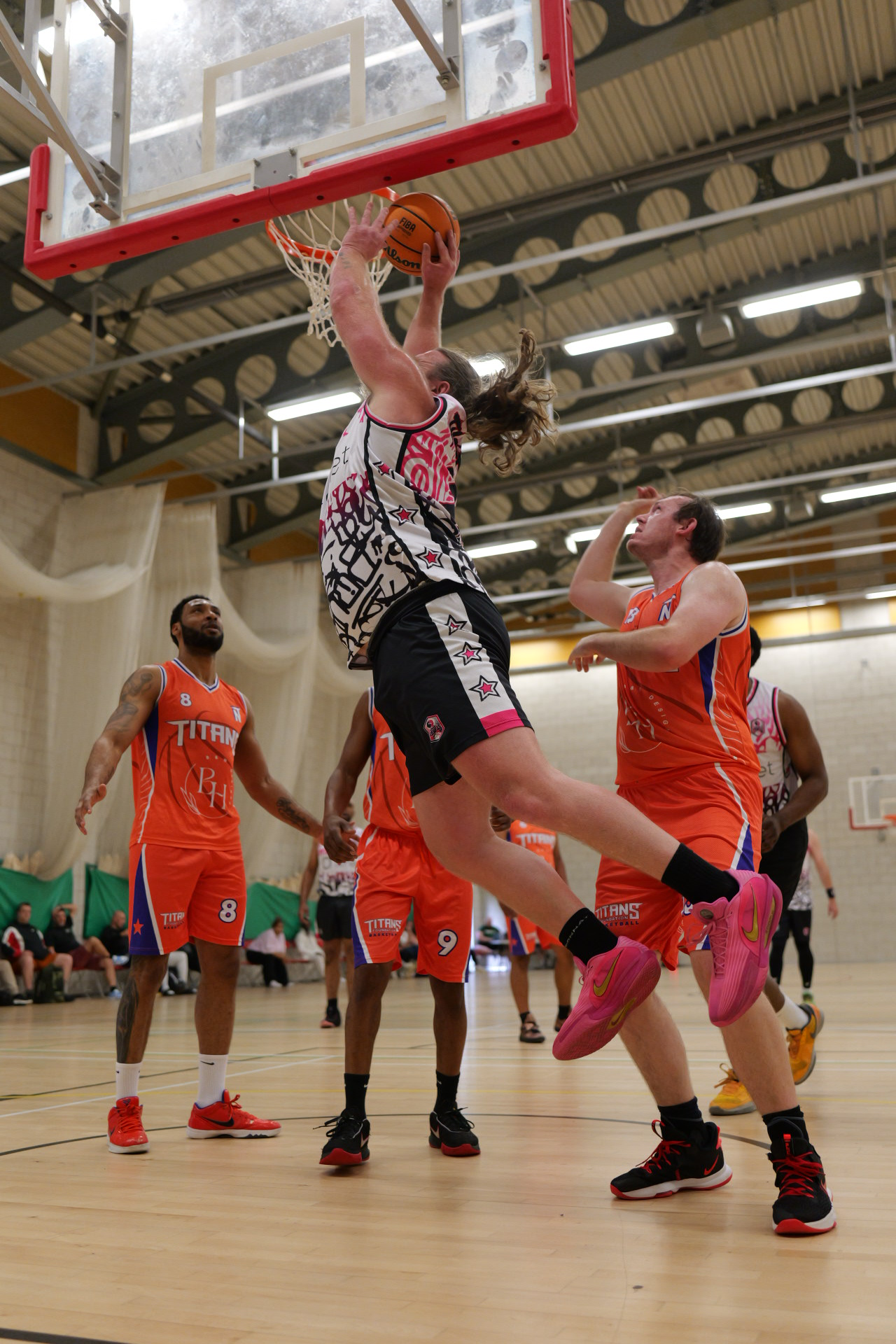 Women’s basketball game, player in black shoots under the hoop as defenders in orange contest.