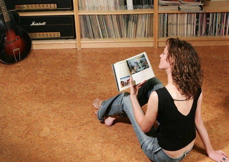 Femme assise sur un sol en liège consultant un magazine, pièce avec étagères à disques.
