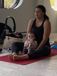 Une femme est assise sur un tapis de yoga et tient un bébé.