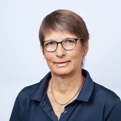Eine Frau mit Brille und blauem Hemd lächelt in die Kamera.