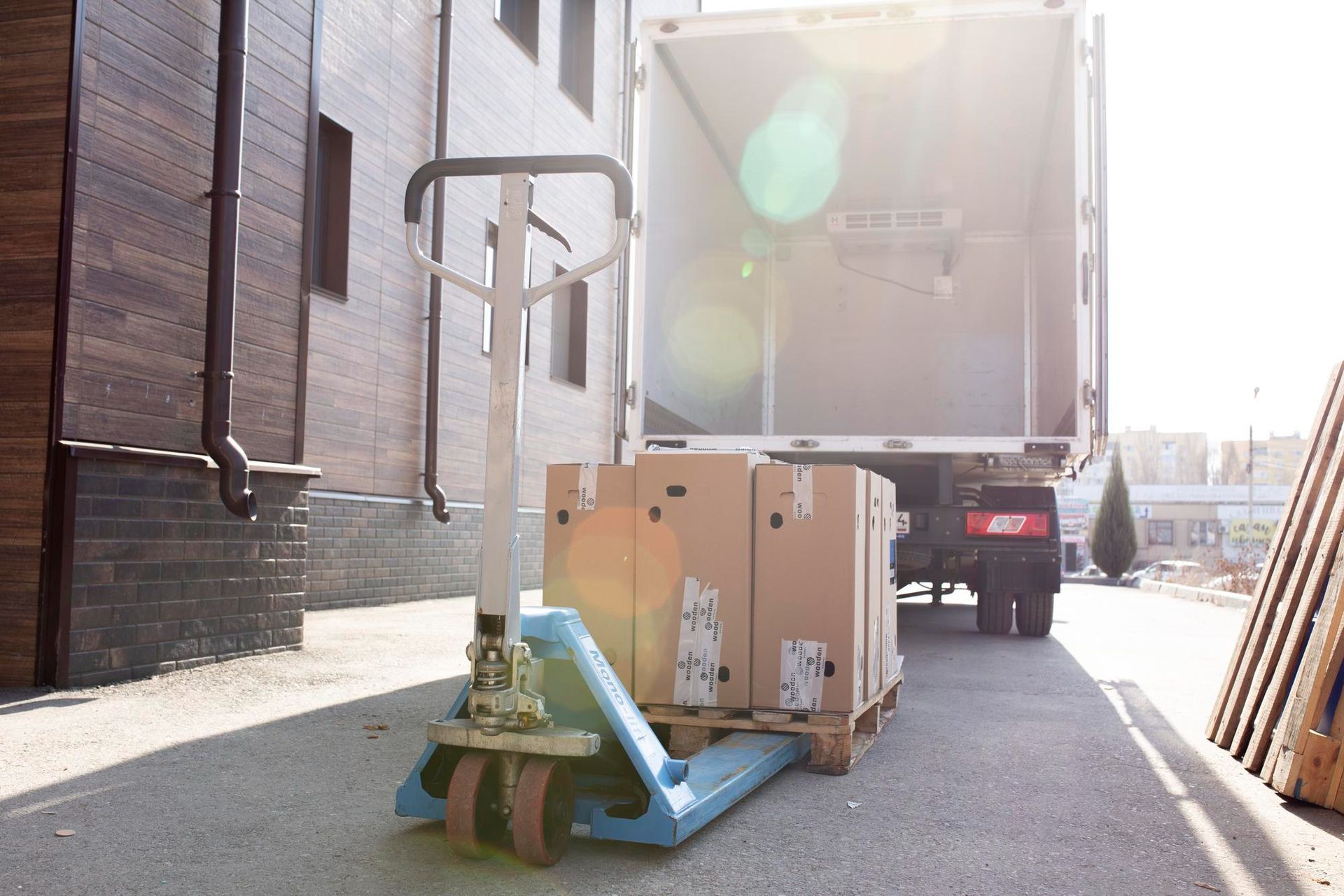 Hand truck with boxes on a pallet being loaded into a truck in a sunny outdoor setting.
