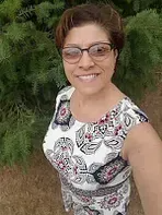 Woman smiling, wearing glasses and a floral print dress, posing outdoors.