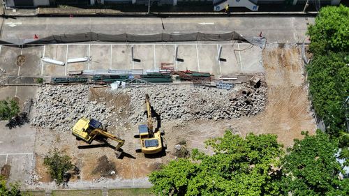 Aerial view of a construction site with two yellow excavators clearing rubble beside a partially demolished wall.