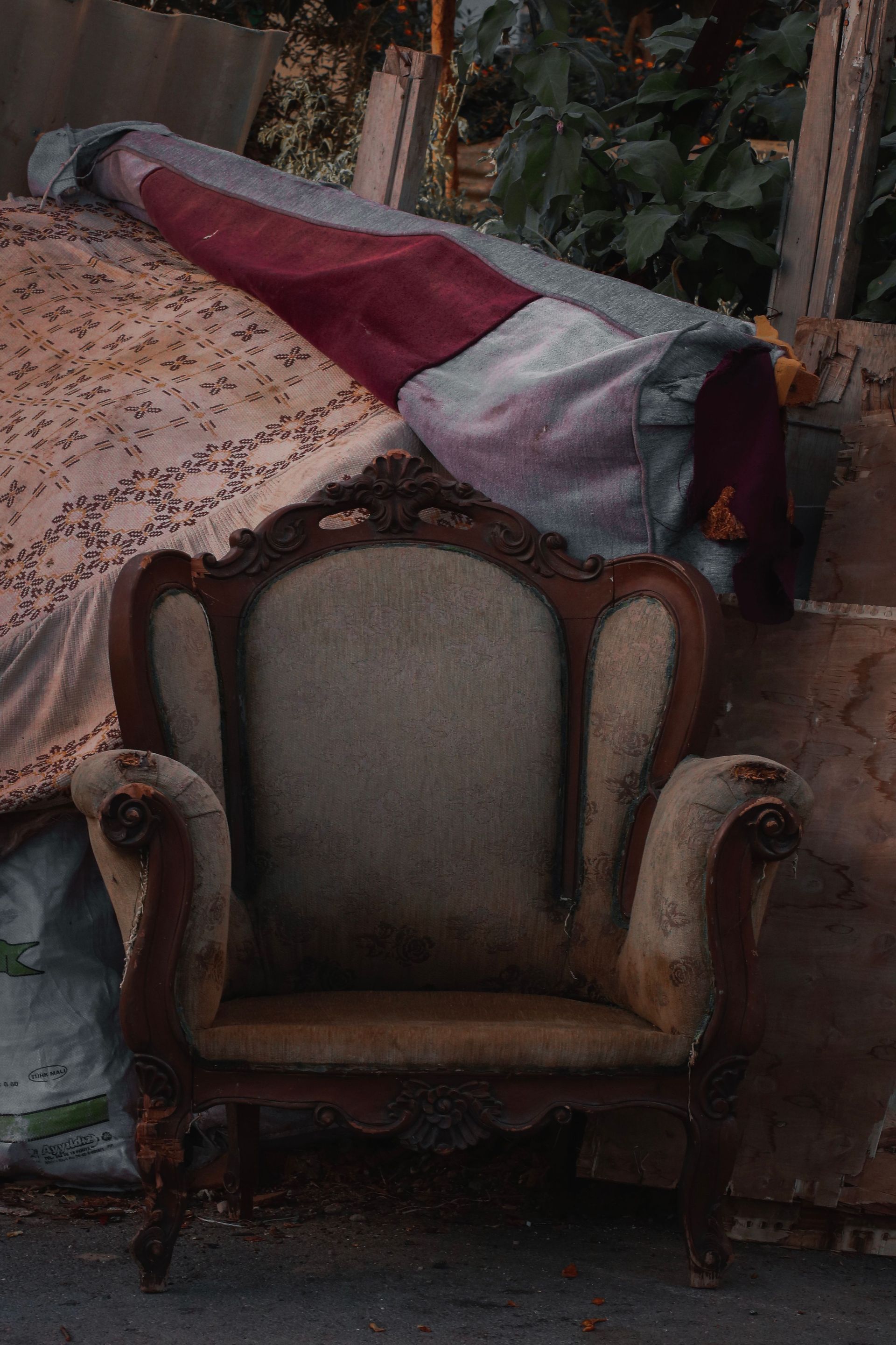 An ornate armchair draped with a maroon and white cloth, sitting outdoors in a cluttered area.