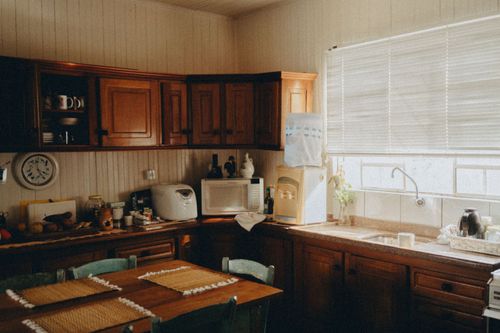Warm wooden kitchen with cabinets, dining table, and sunlit window above a sink.