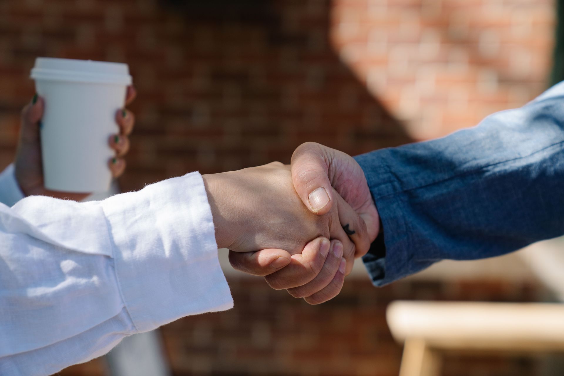 Two people shaking hands outdoors, one holding a white coffee cup