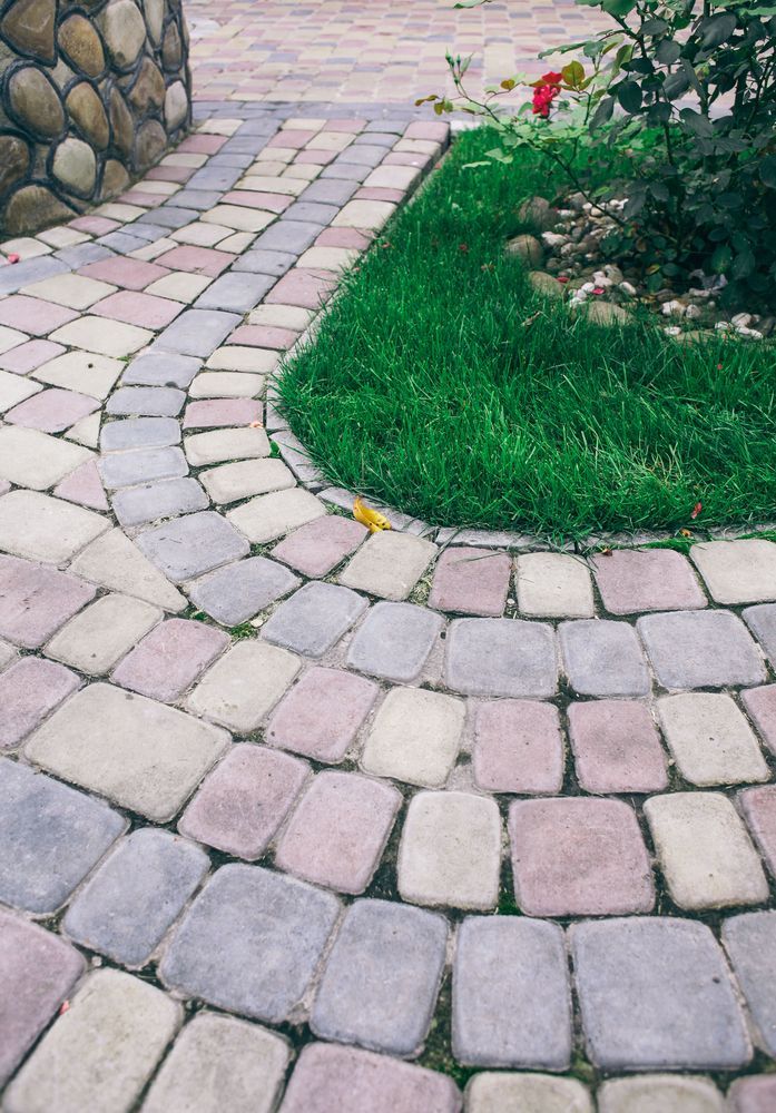 Curved stone paver path beside a green lawn and garden bed with flowers