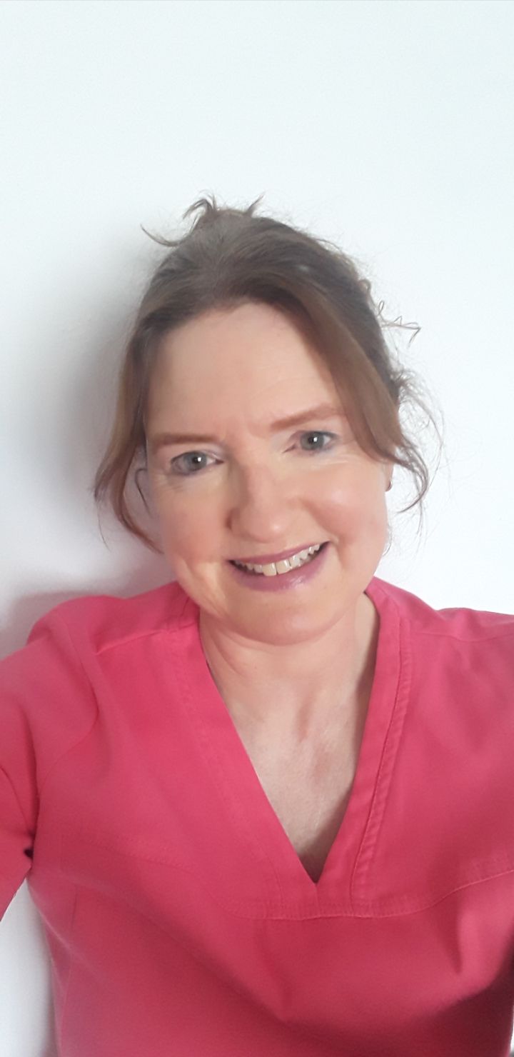 A woman in a pink scrub top is smiling for the camera.