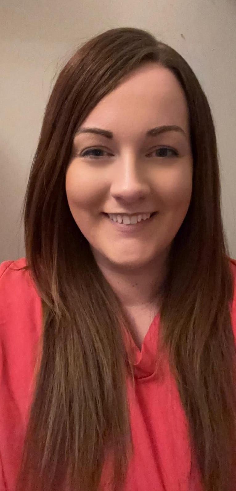 A woman with long brown hair is wearing a red shirt and smiling.