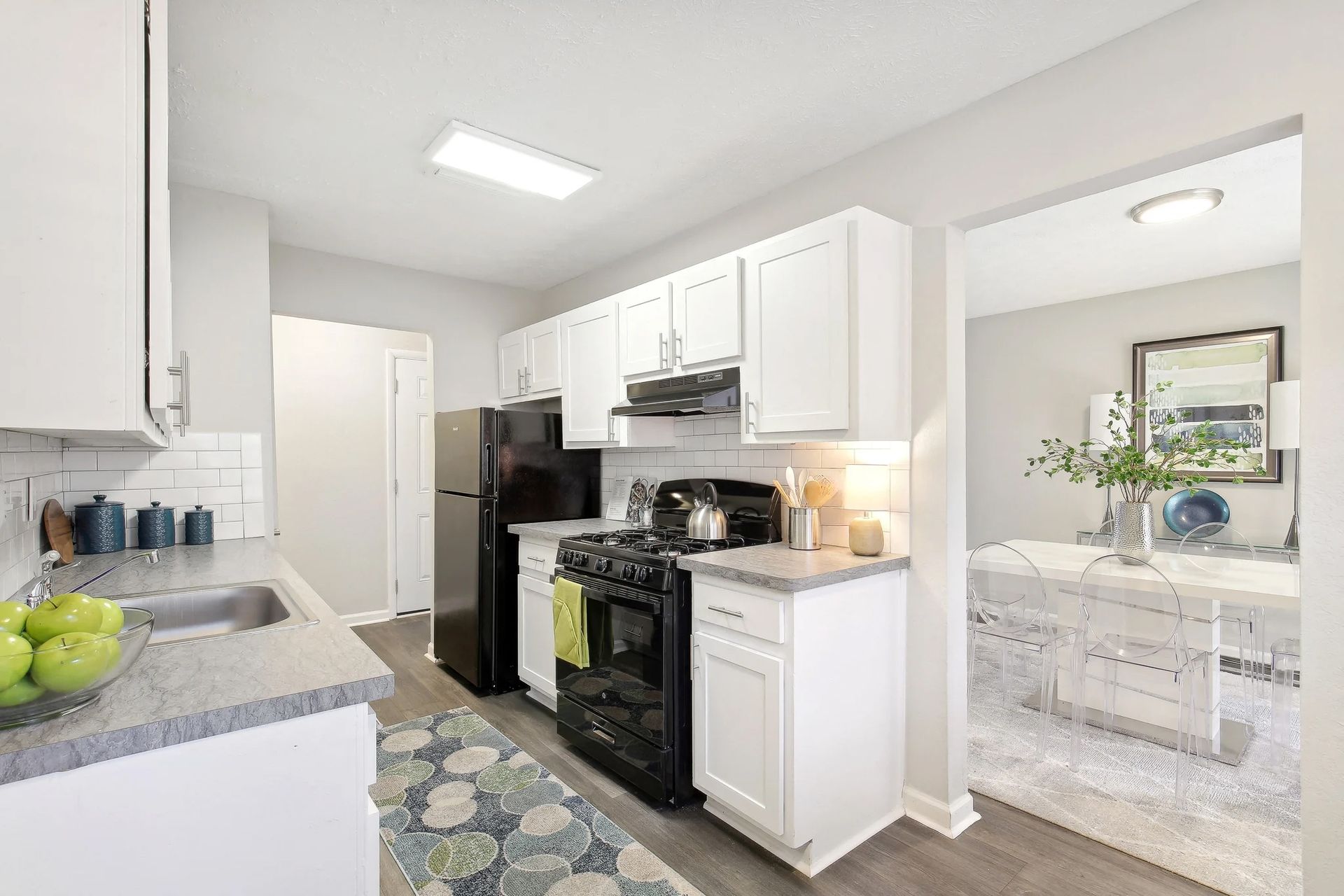 A kitchen with white cabinets , a black stove , a refrigerator , and a sink.