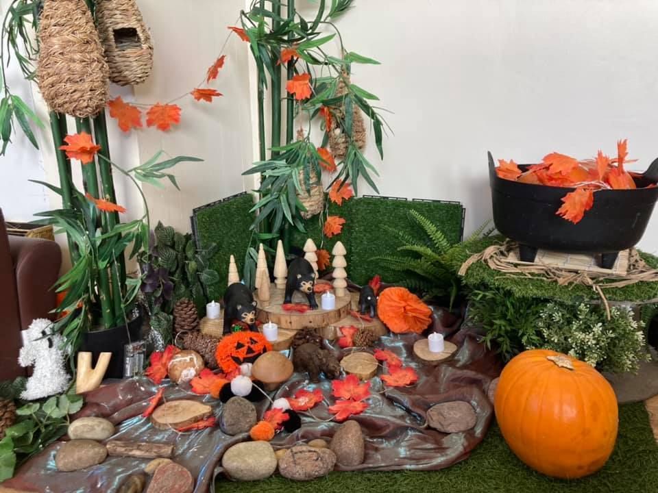 A table with a pumpkin , candles , and a cauldron filled with orange leaves.