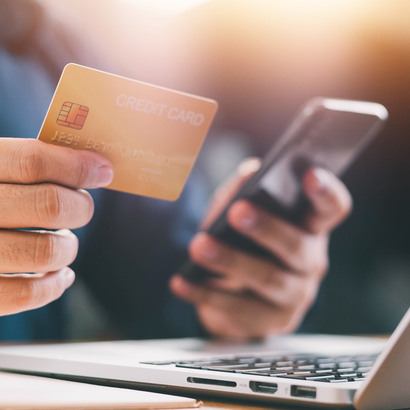 A person is holding a credit card and a cell phone in front of a laptop.
