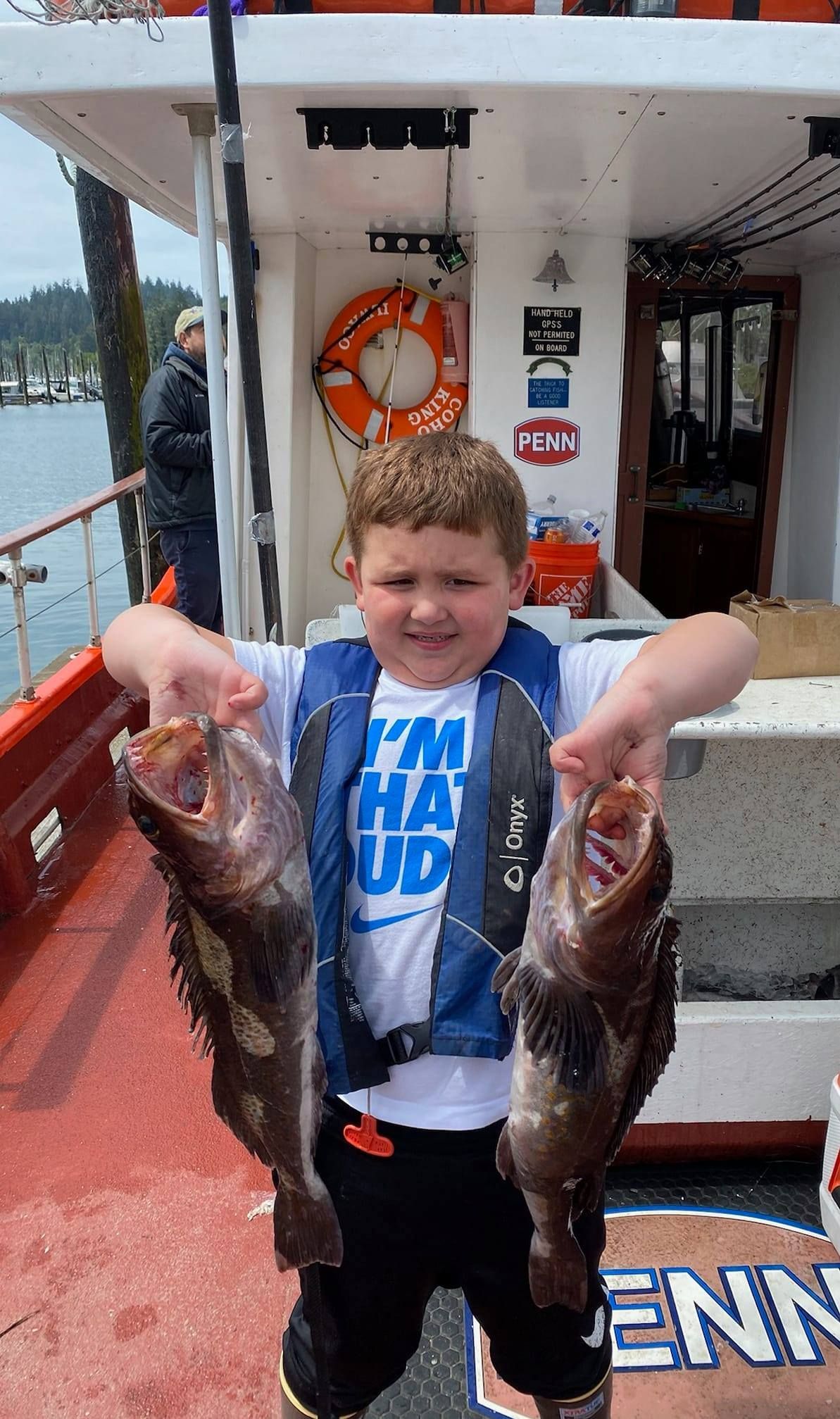 A young boy is holding two fish in his hands on a boat.