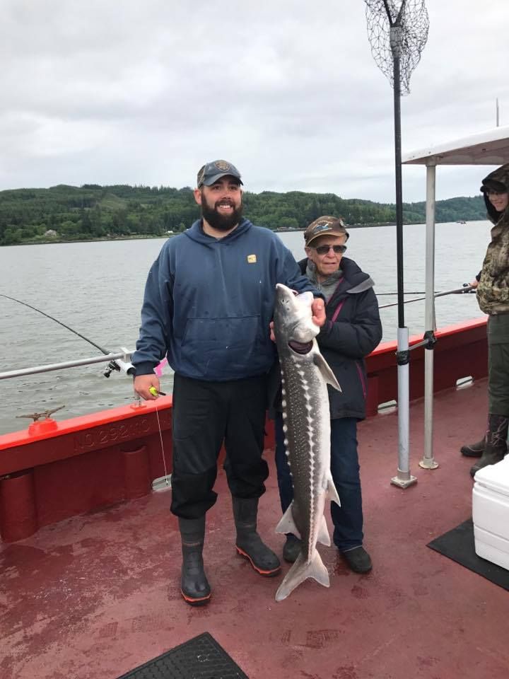 Two men are standing on a boat holding a large fish.