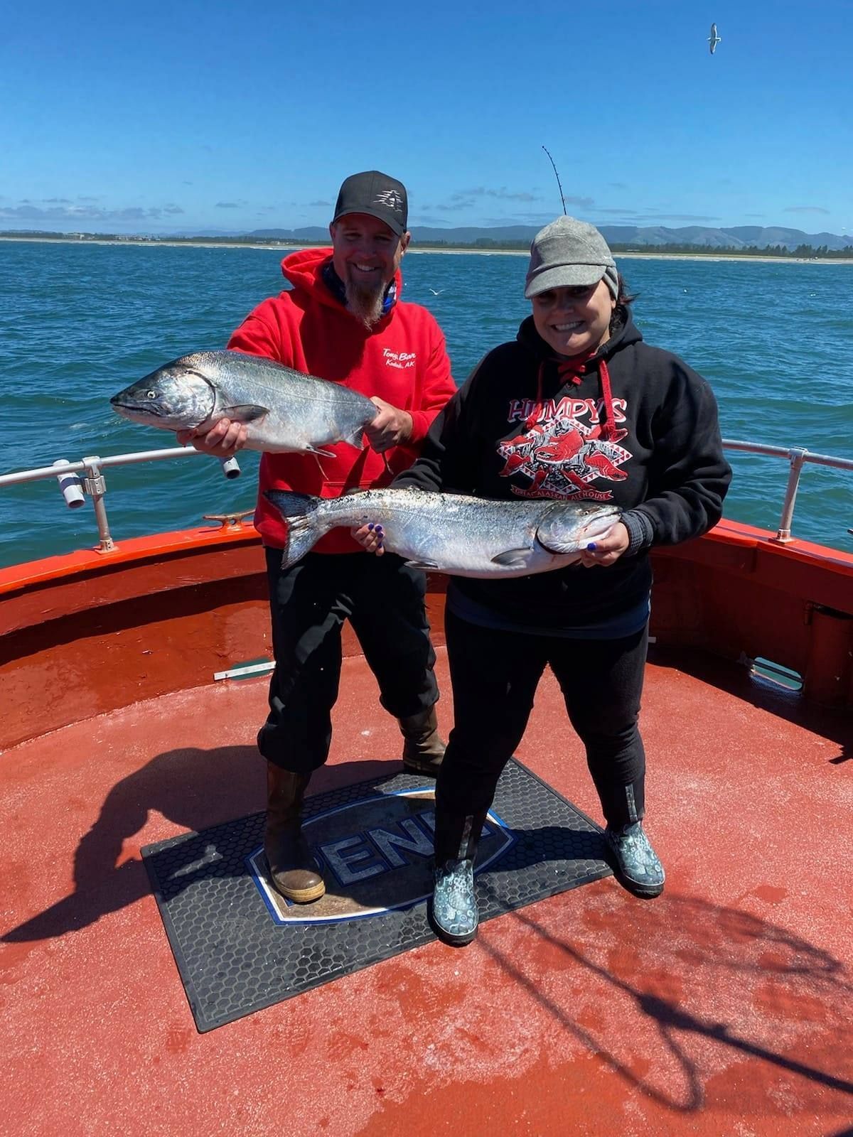 A man and a woman are holding two fish on a boat.