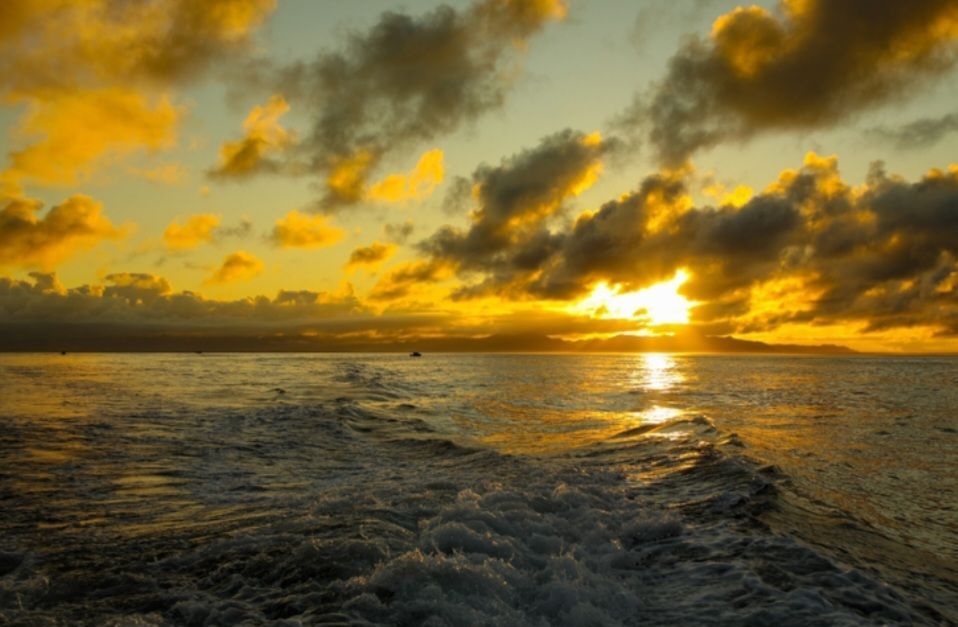 The sun is setting over the ocean with a boat in the distance.