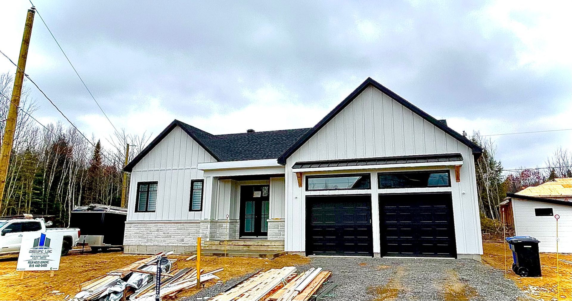 Une maison blanche avec des portes de garage noires est en construction.