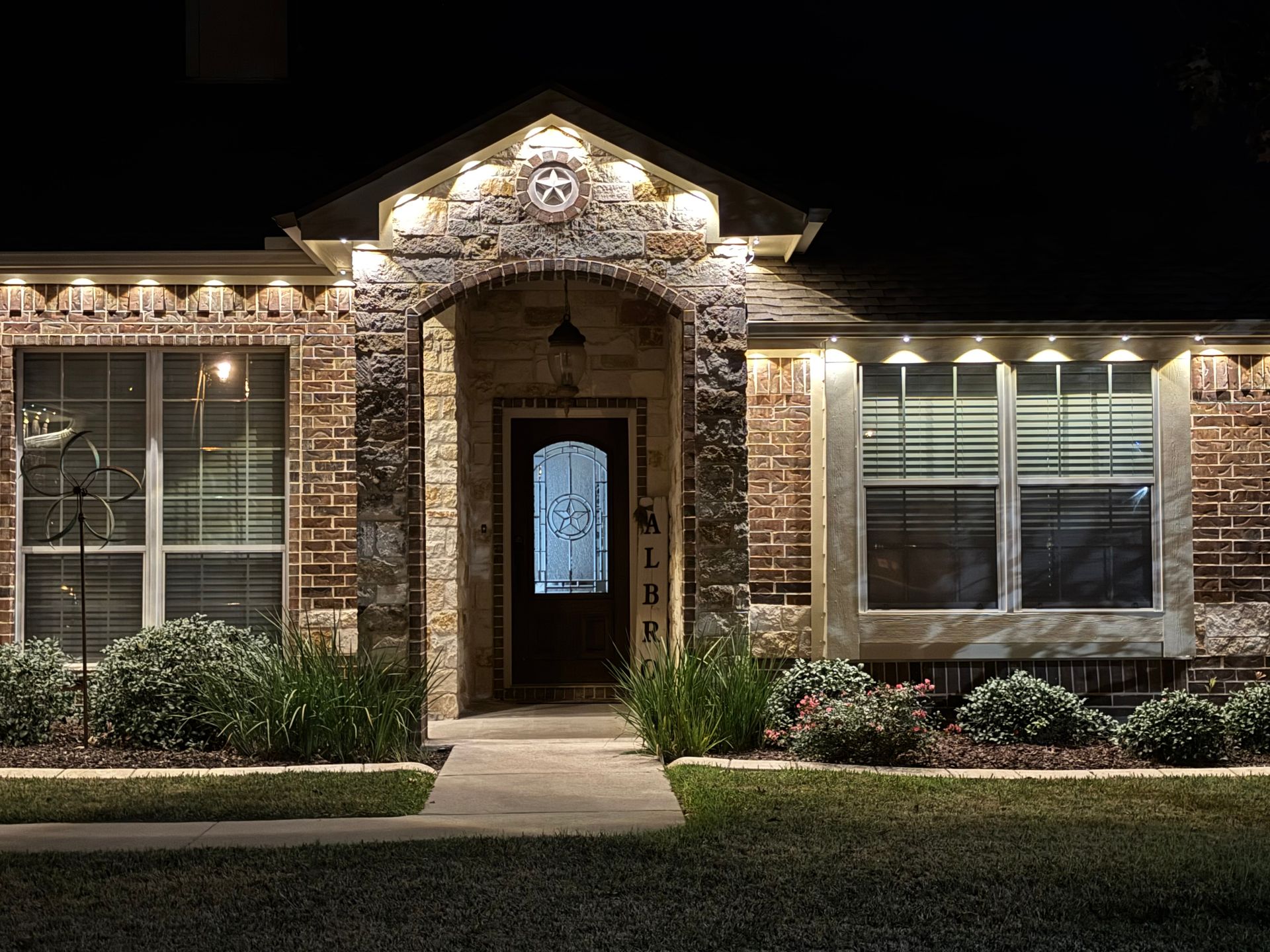 Well-lit brick house exterior at night with a front walkway and lit windows