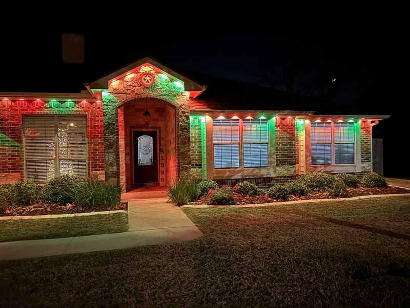 House decorated with red and green holiday lights at night, with lit windows and a front walkway.