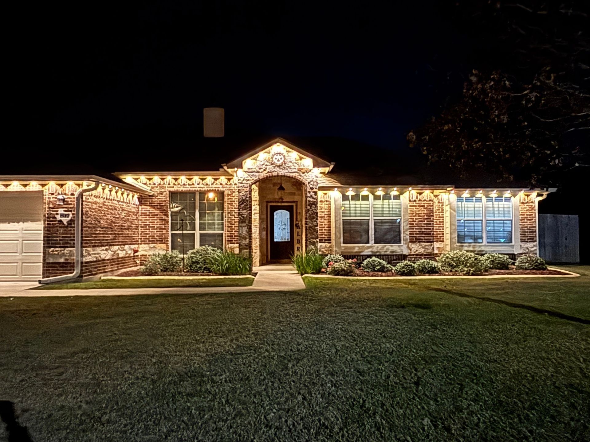 Brick house with warm Christmas lights and a lit walkway at night