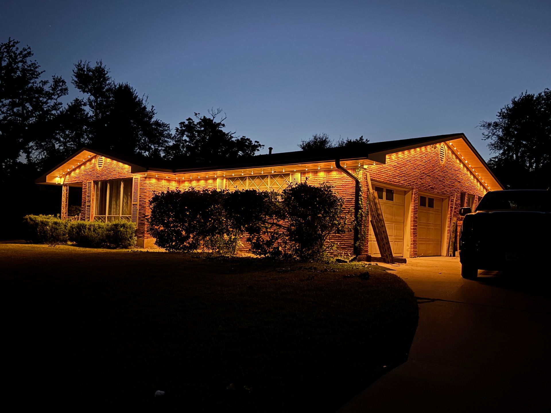 Single-story house outlined in warm white lights at night, with a lit porch and dark yard.