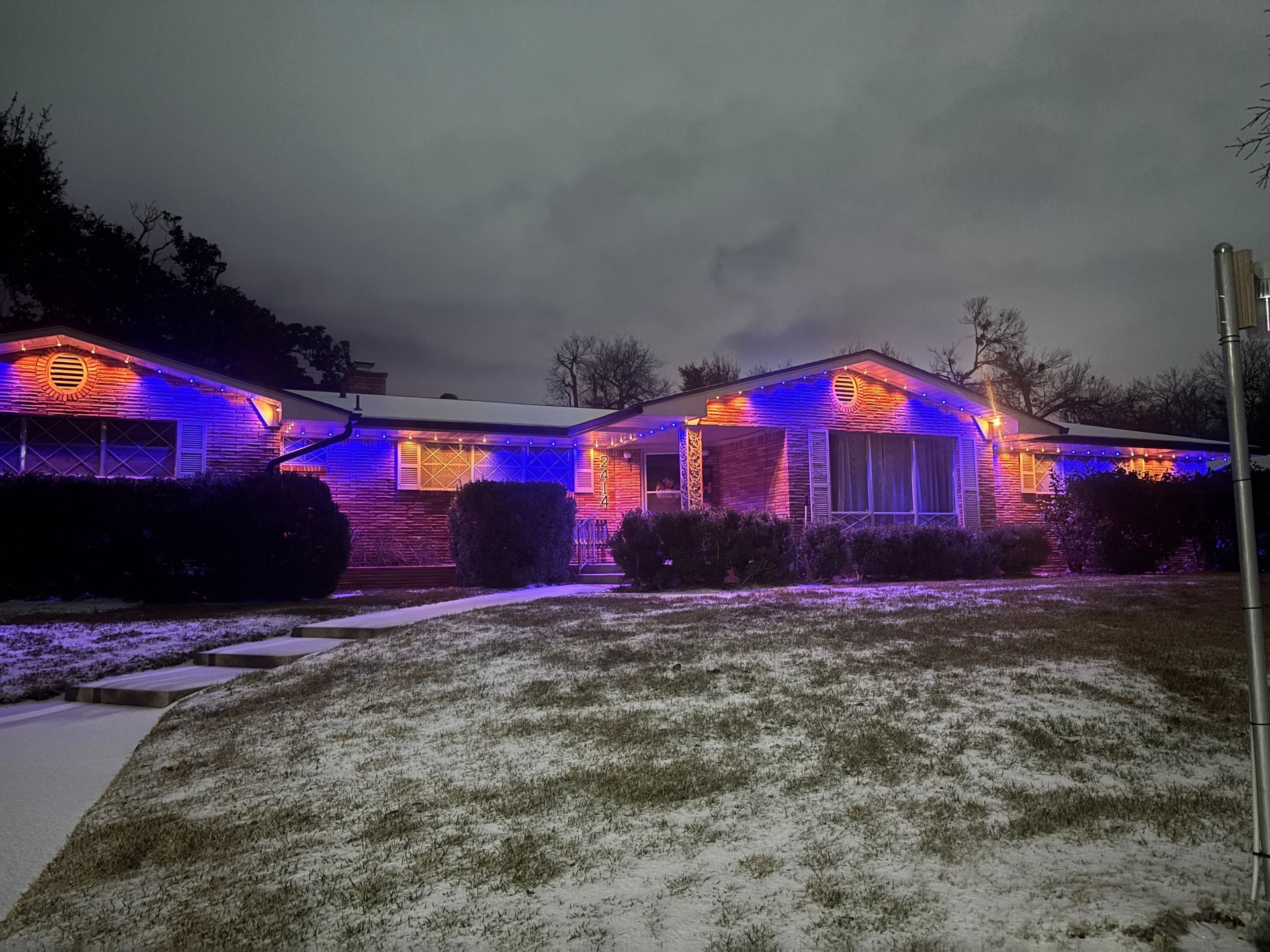 Suburban house at dusk glowing with purple and orange holiday lights under a cloudy sky