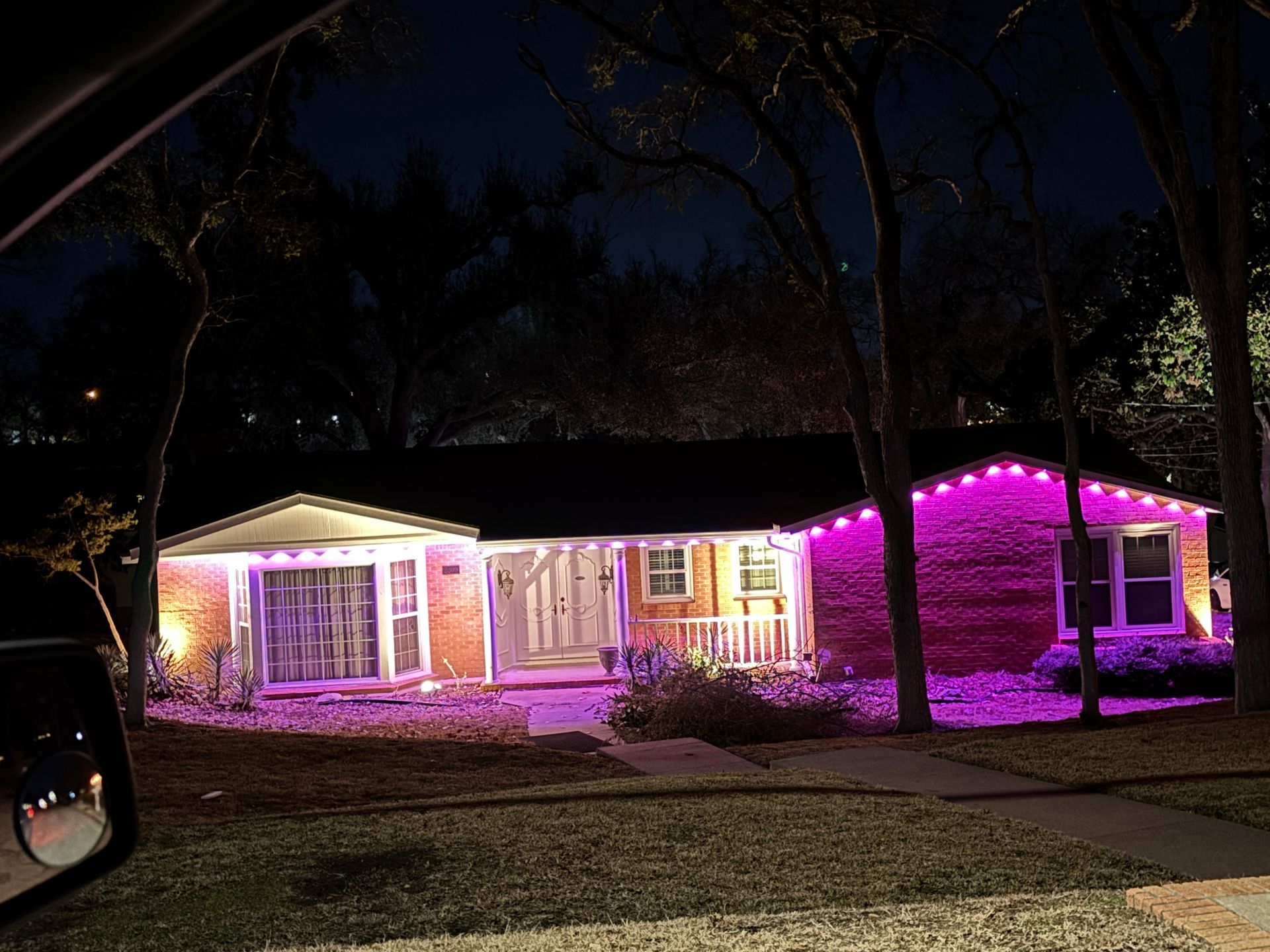 House lit with pink and white lights at night, viewed from the street