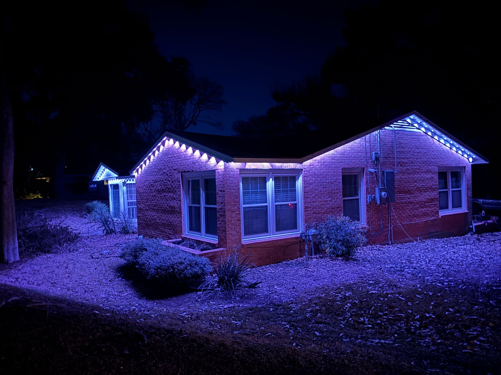 Brick house outlined with purple holiday lights at night, with snow on the ground and roof.