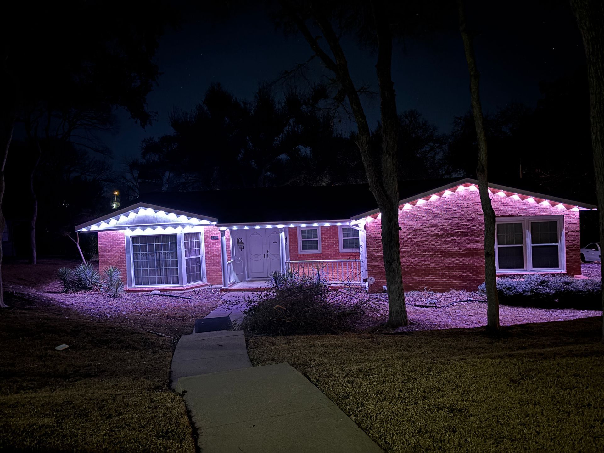 Single-story house lit with pink and white lights at night, with a walkway leading to the front door
