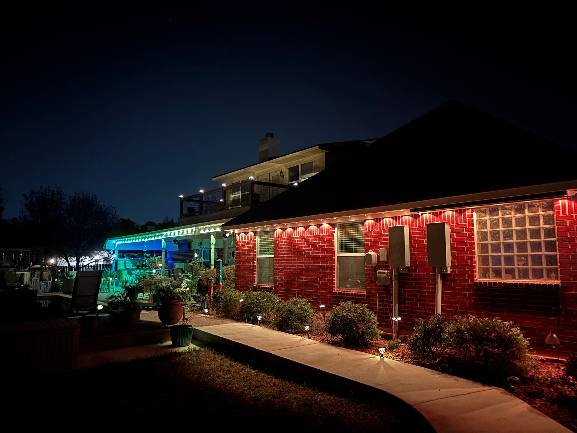 Nighttime view of a brick building lit with red and blue lights, with a walkway and shrubs in front.