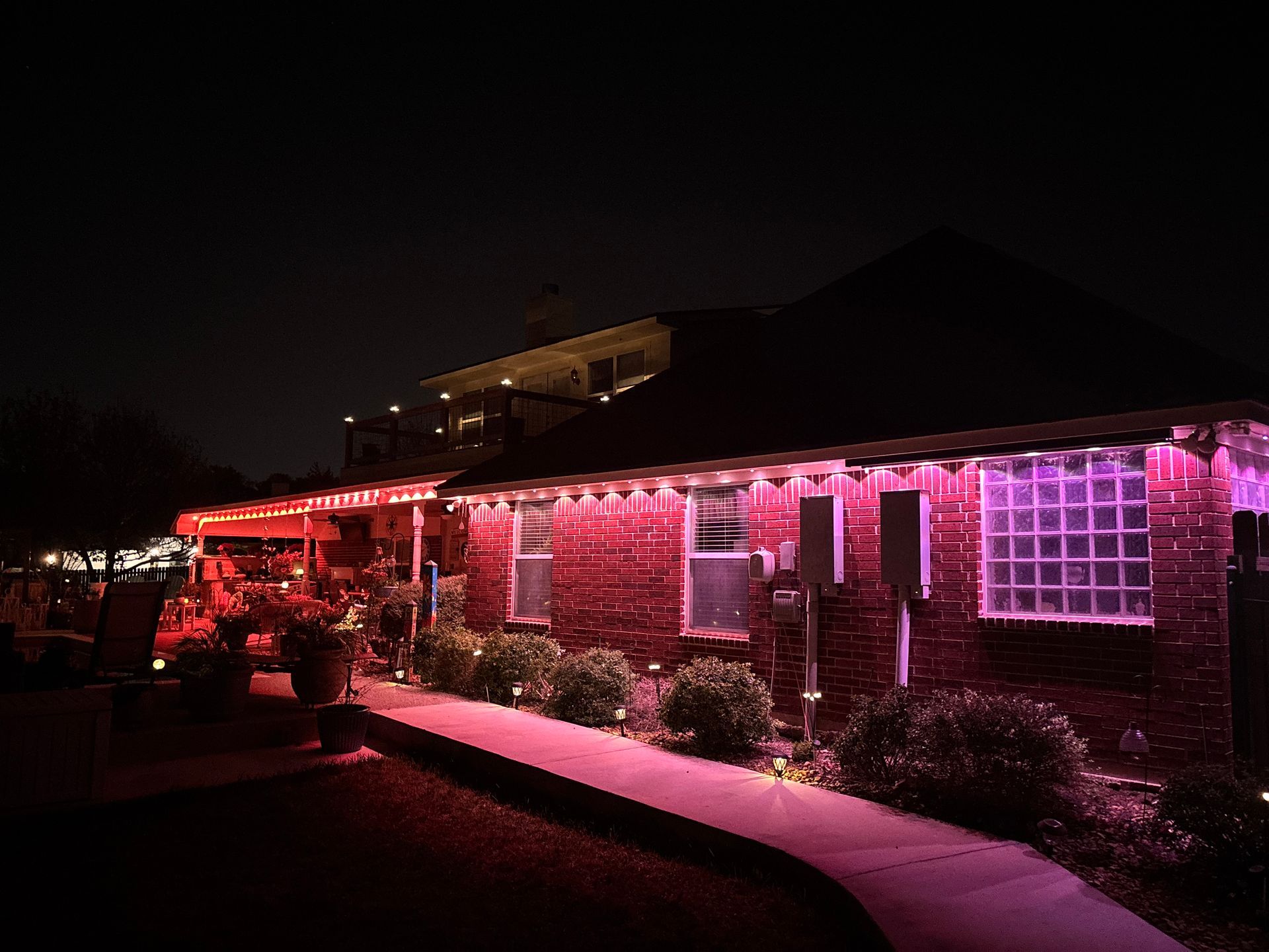 House lit with red and pink lights at night, with shrubs along a walkway