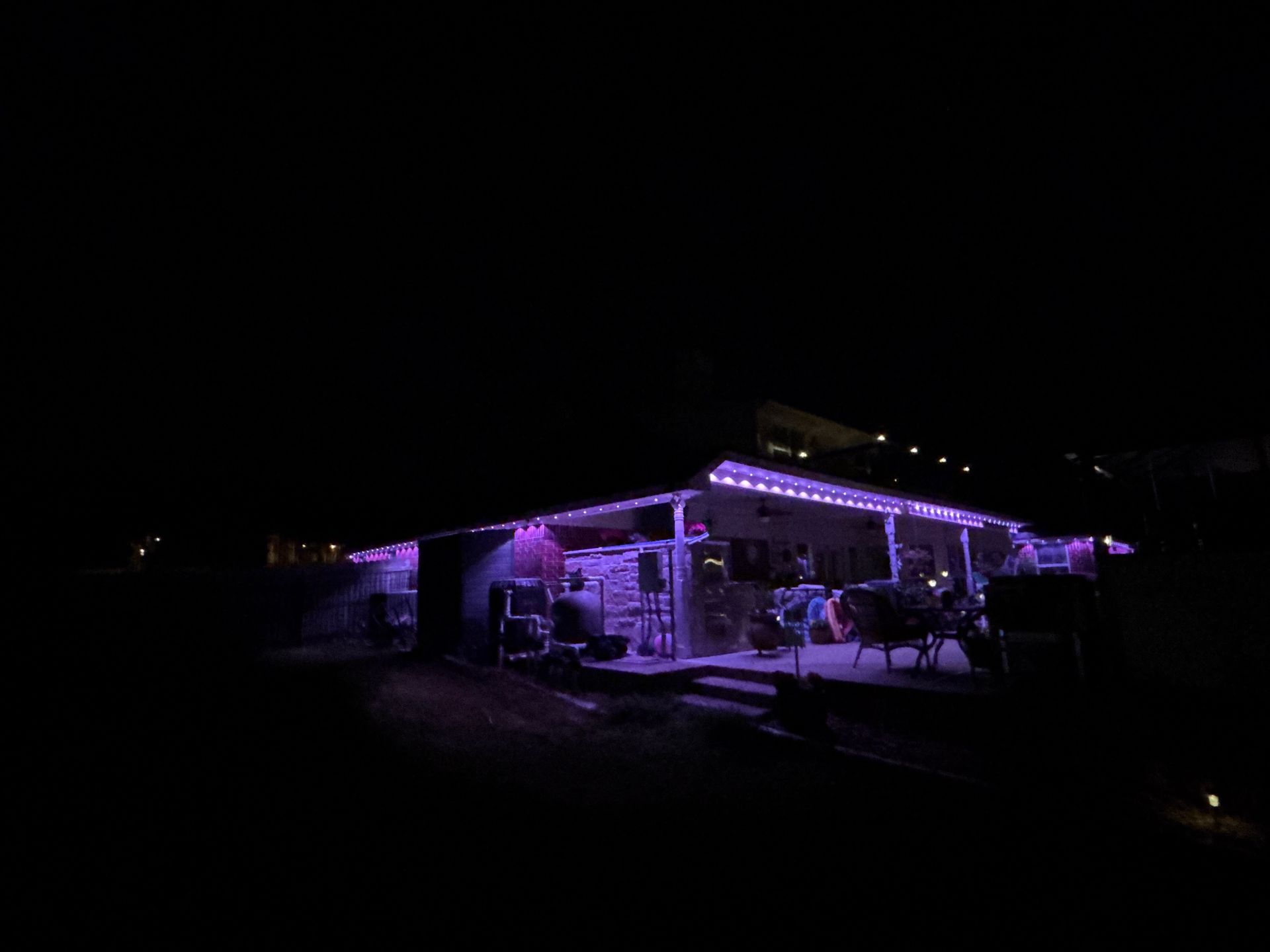 A house at night lit with purple lights, with people gathered on the porch.