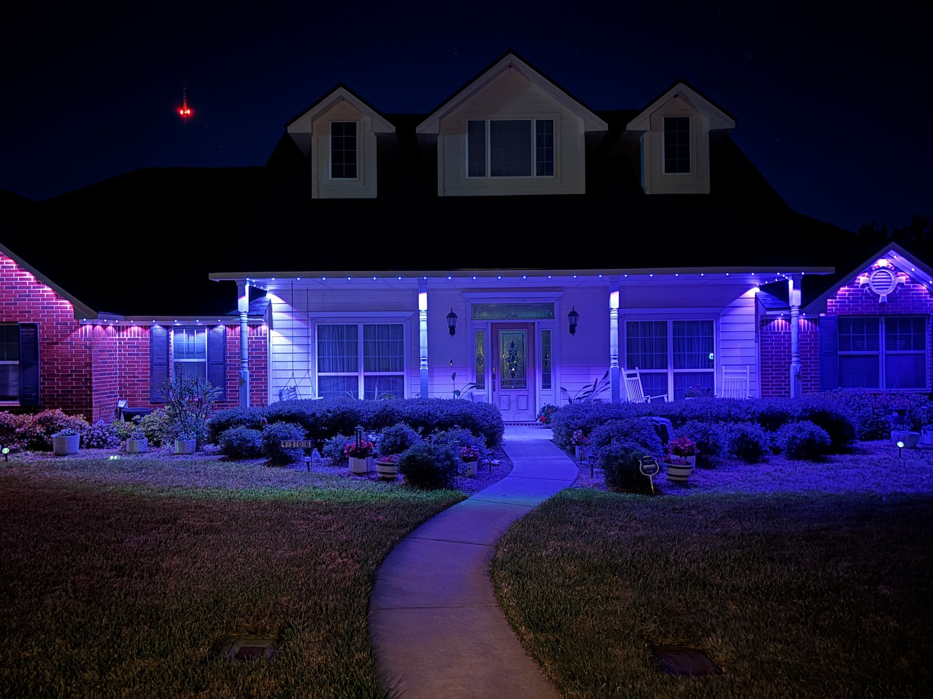 House lit with blue and purple lights at night, with a curved walkway leading to the front door.