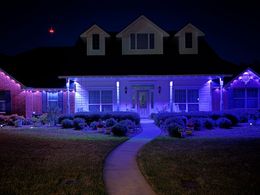House lit in blue and purple holiday lights at night, with a curved walkway leading to the front door