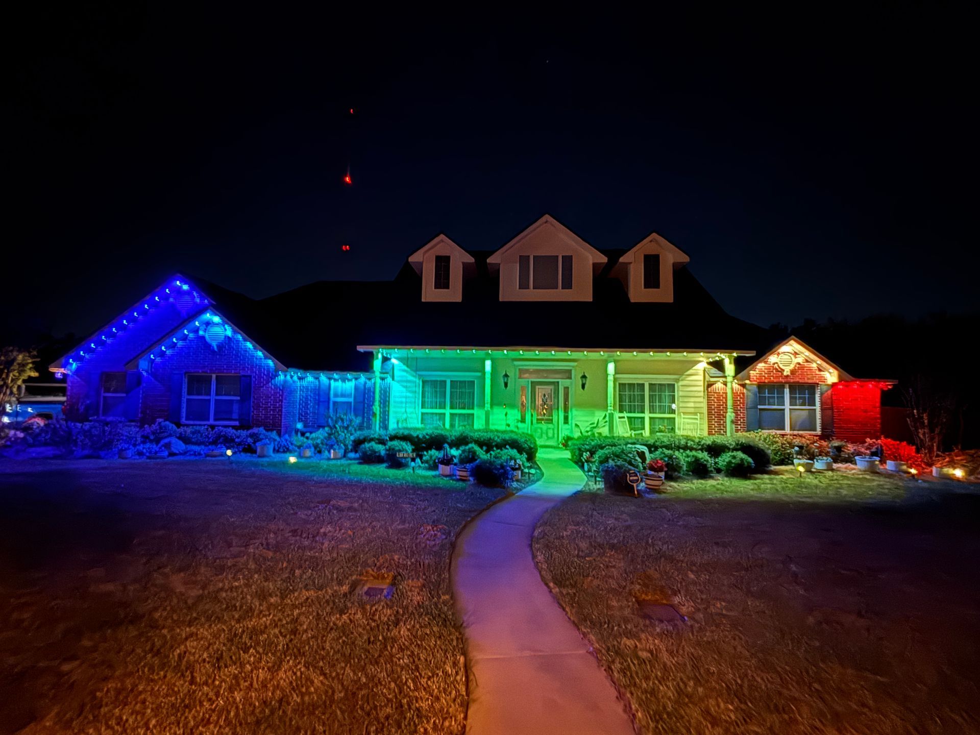 House lit with rainbow Christmas lights at night, with a curved walkway leading to the front door.