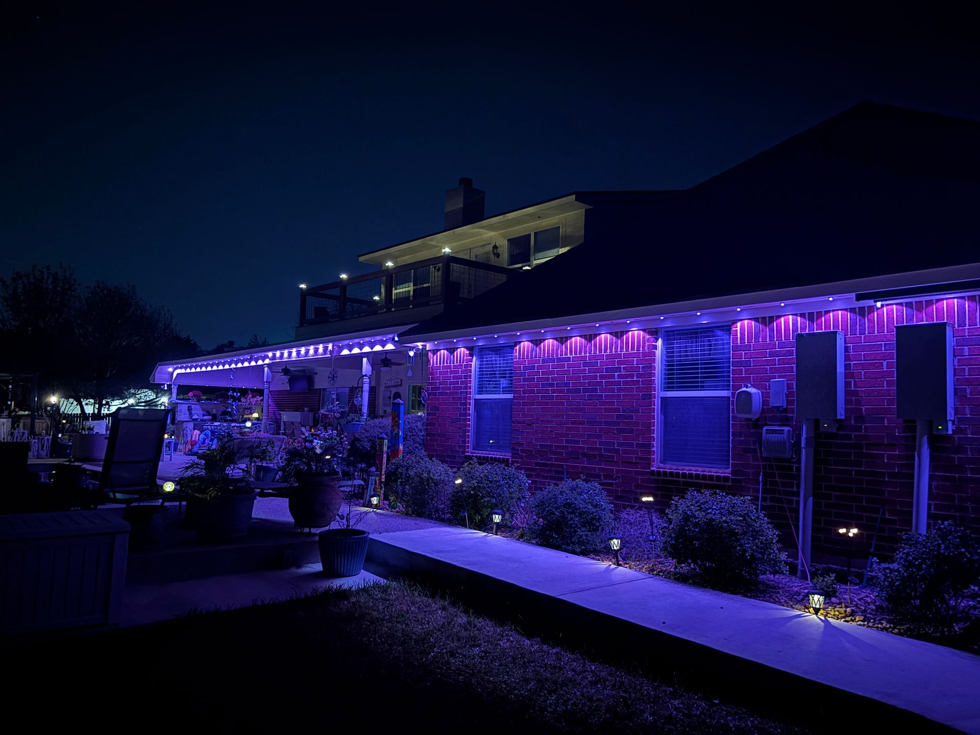 House exterior at night lit with purple and blue string lights along the porch and roofline.