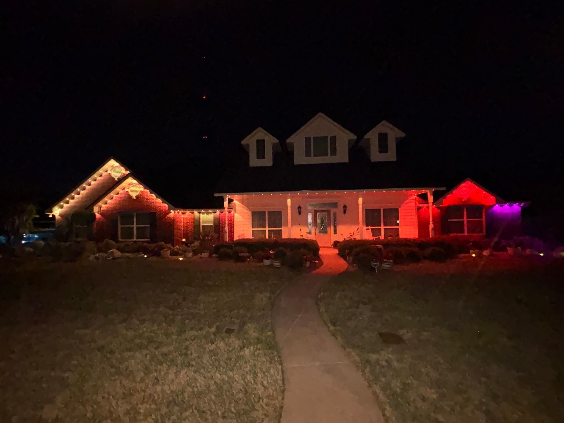 House decorated with colorful Christmas lights at night, viewed from a front walkway.