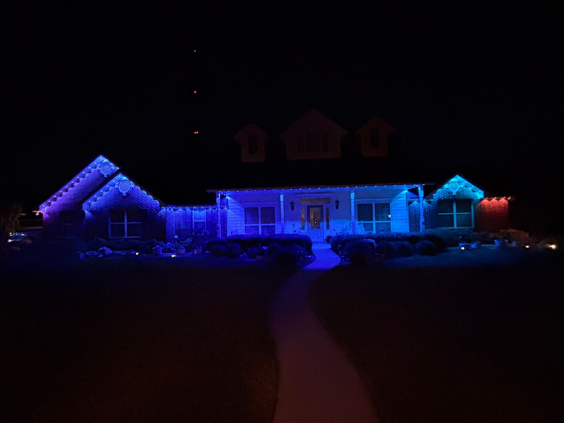House outlined in blue and purple holiday lights at night, with a lit walkway leading to the front door