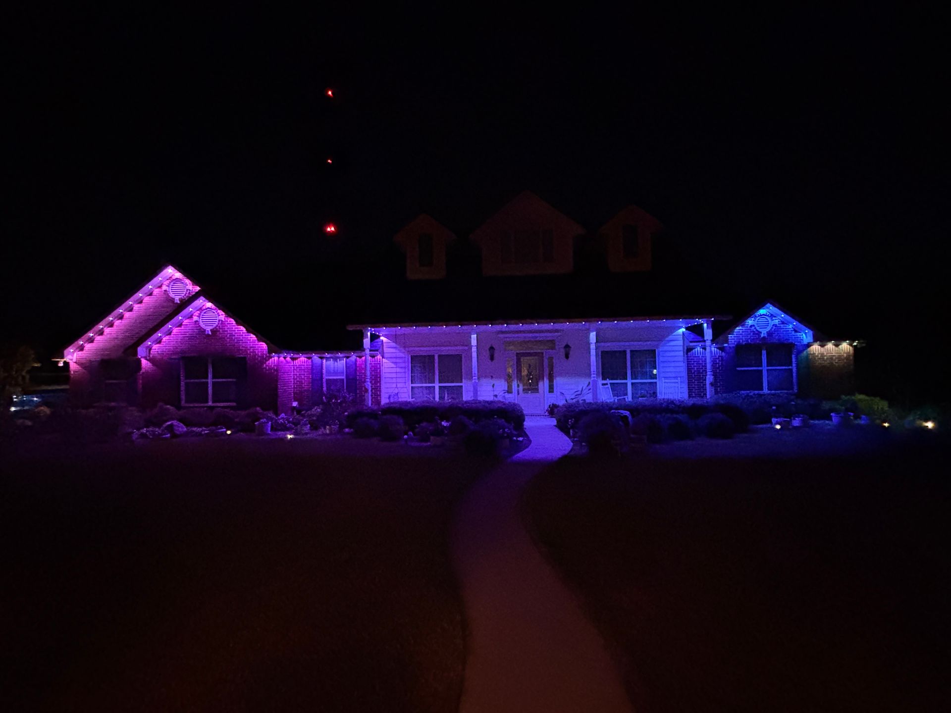 House lit in purple and blue at night, with a dark lawn and curved walkway leading to the front door