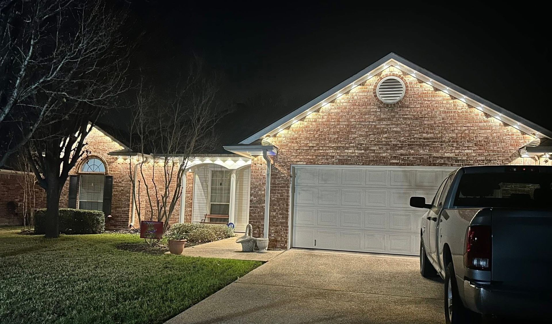 Brick house with lit holiday lights, a garage, and a parked SUV at night