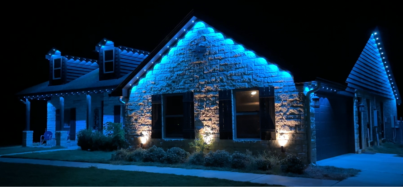 Two-story house at night, lit with green and pink decorative lights at the entrance and roofline.