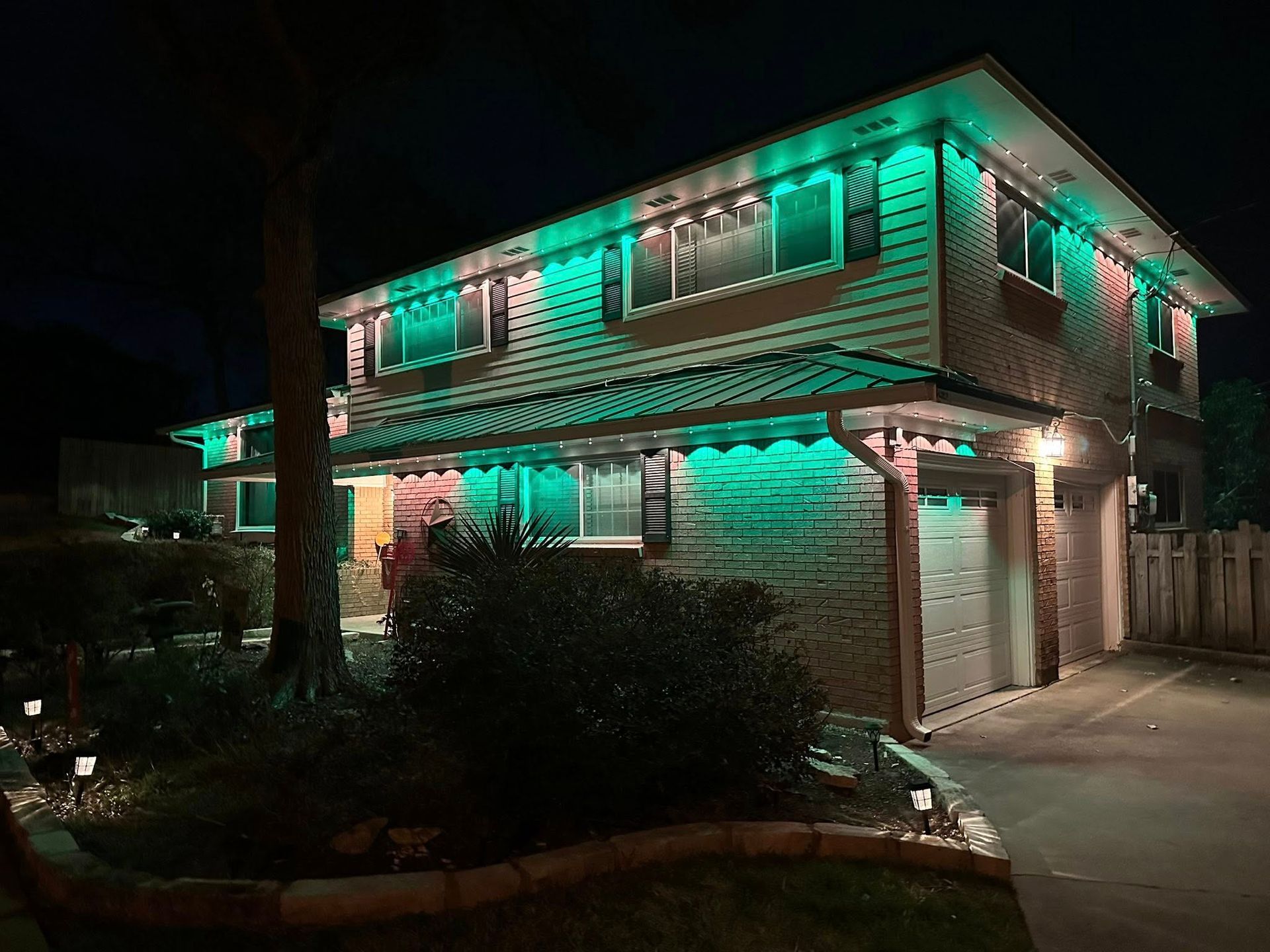 Two-story house at night, lit with green and pink decorative lights at the entrance and roofline.