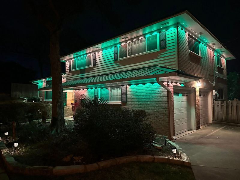 Two-story house at night, lit with green and pink decorative lights at the entrance and roofline.