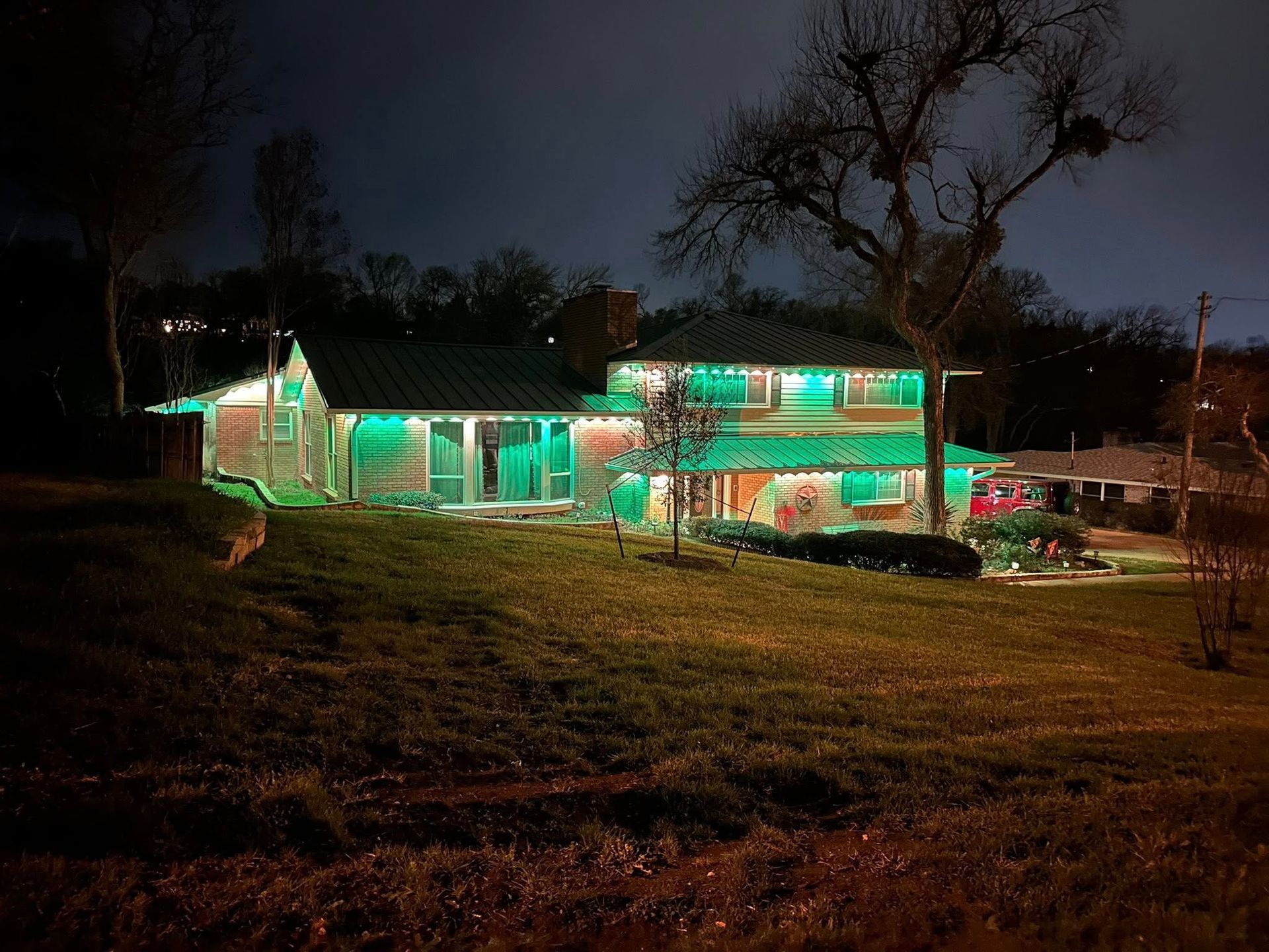 House lit with green holiday lights at night on a dark hillside.