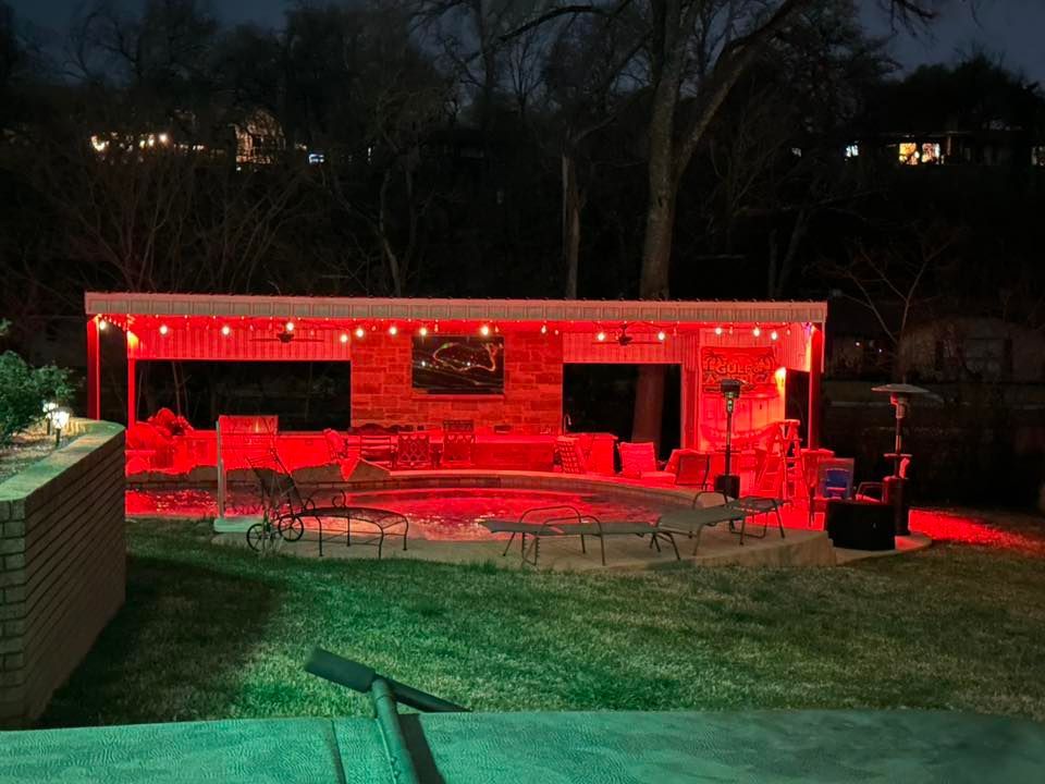 Backyard patio lit red at night, with outdoor seating and a fire pit by a house